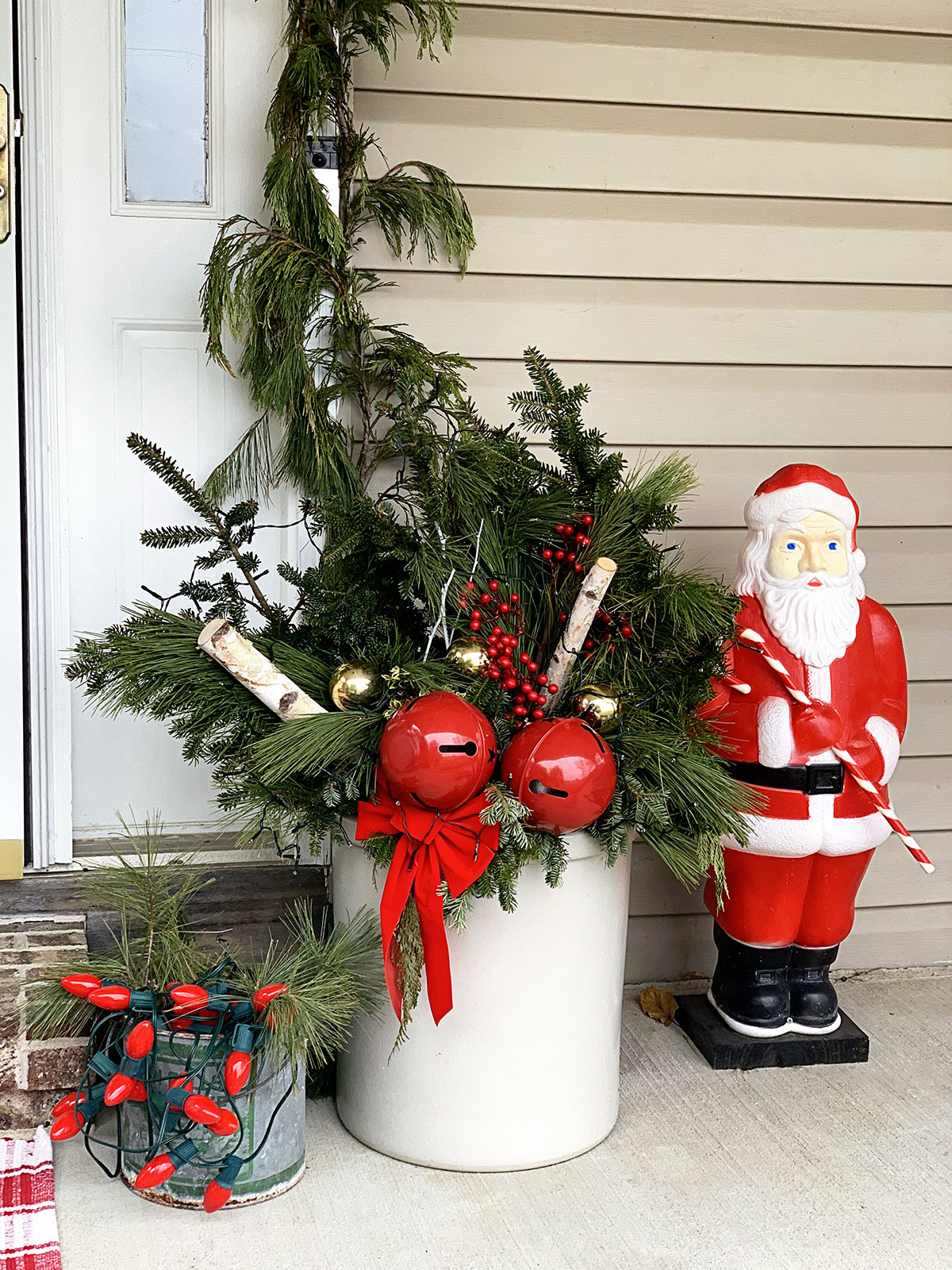 Christmas greenery in a crock setting on the front porch along with a blowmold Santa and some red Christmas lights. 