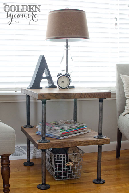 Industrial pipe side table styled with magazines, a lamp and a clock