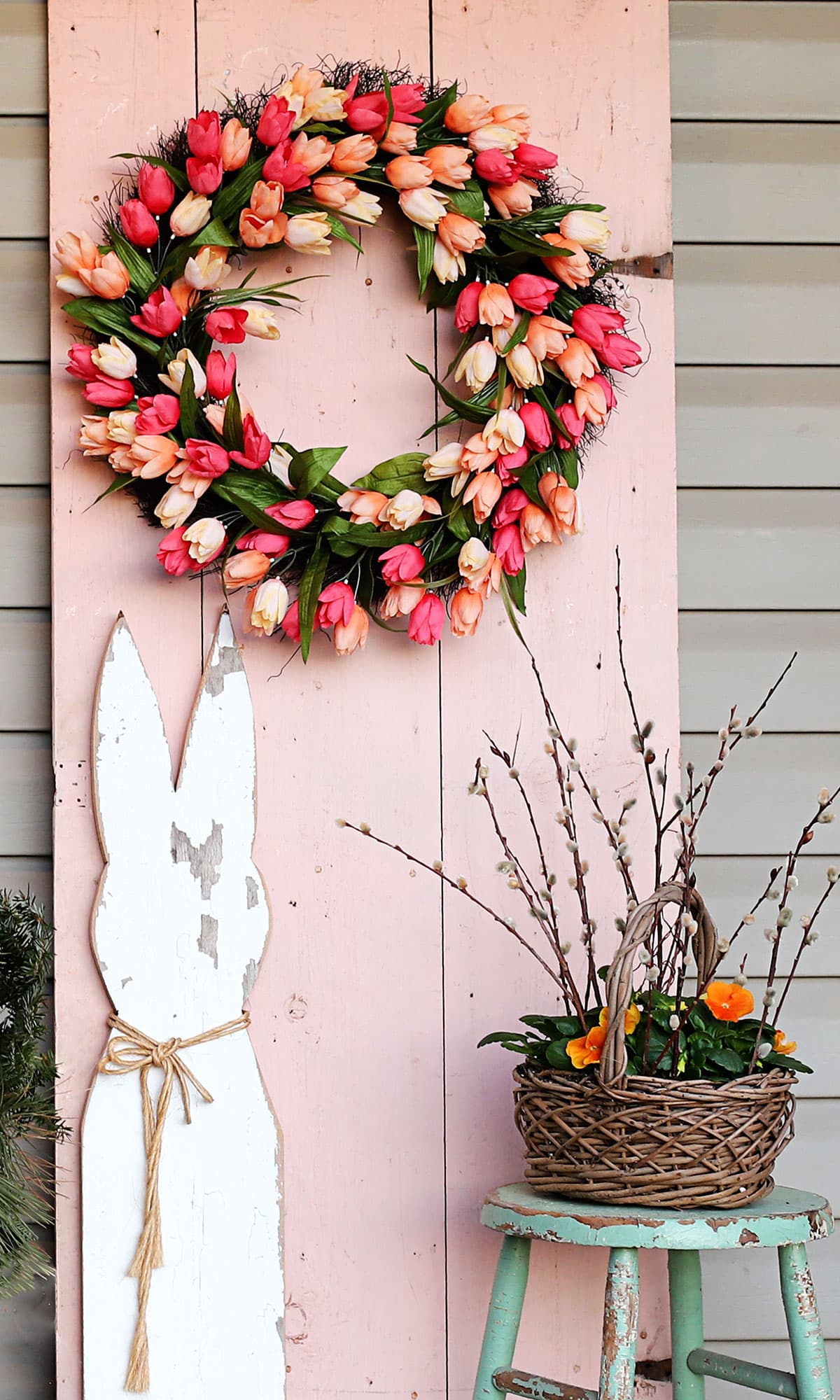 Colorful Easter front porch usinfg repurposed items including a bright pink tulip wreath hung on an old wooden farmhouse door.