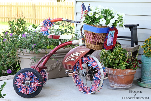 A vintage little red Tricycle decorated for the 4th of July with patriotic crepe papers, flags and flowers. A cute DIY project for patriotic porch decor. 