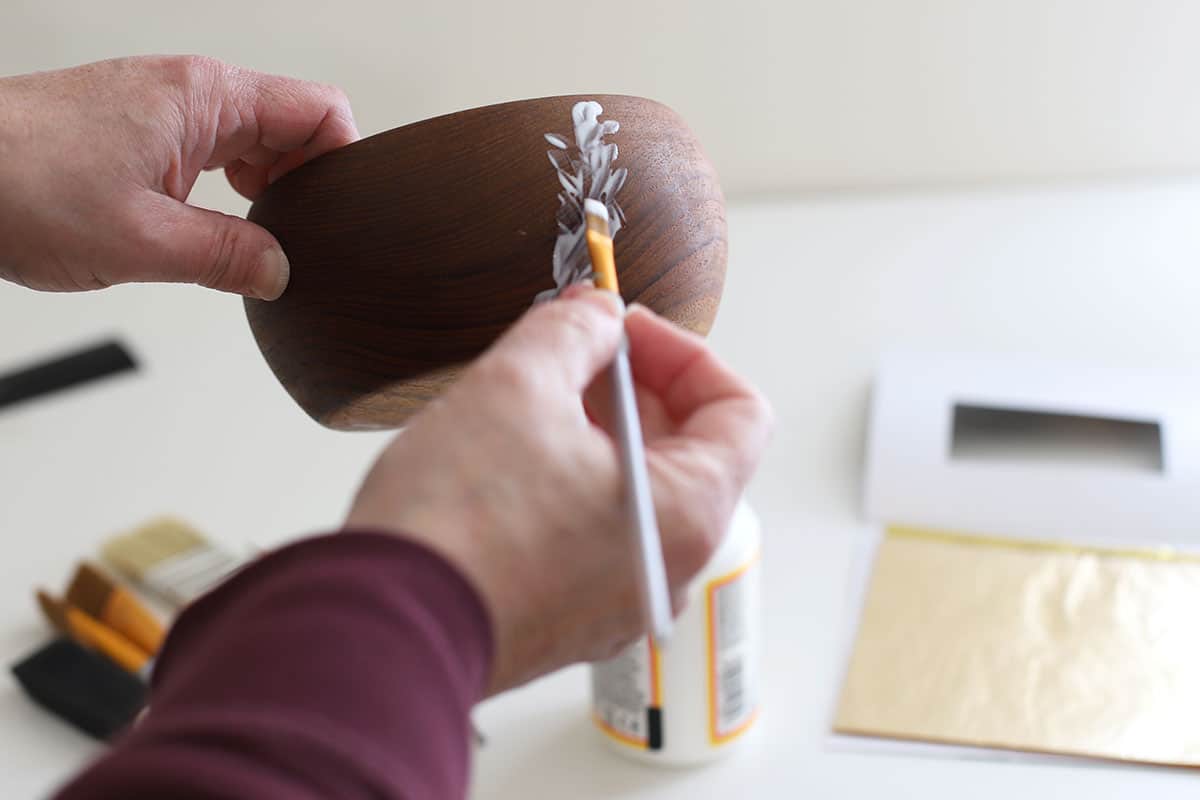 Applying Mod Podge to a wooden bowl in order to add gold leaf.