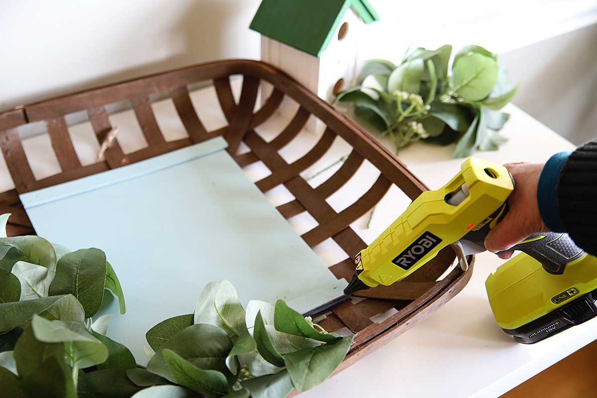 using hot glue gun to adhere eucalyptus leaves to spring basket wreath