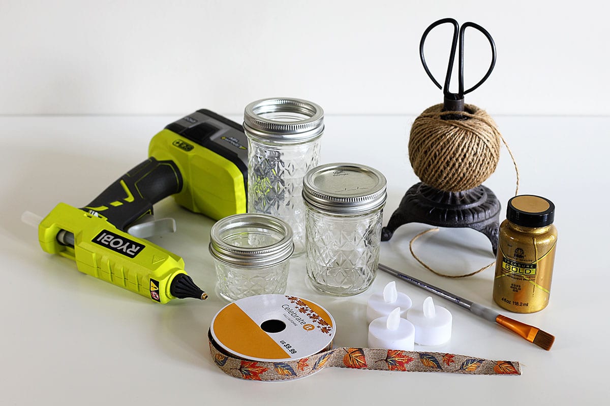 Supplies for making painted mason jar candle holders - Ball jelly jars, metallic gold paint, paintbrush, ribbon, jute twine, scissors, glue gun, battery operated votives.