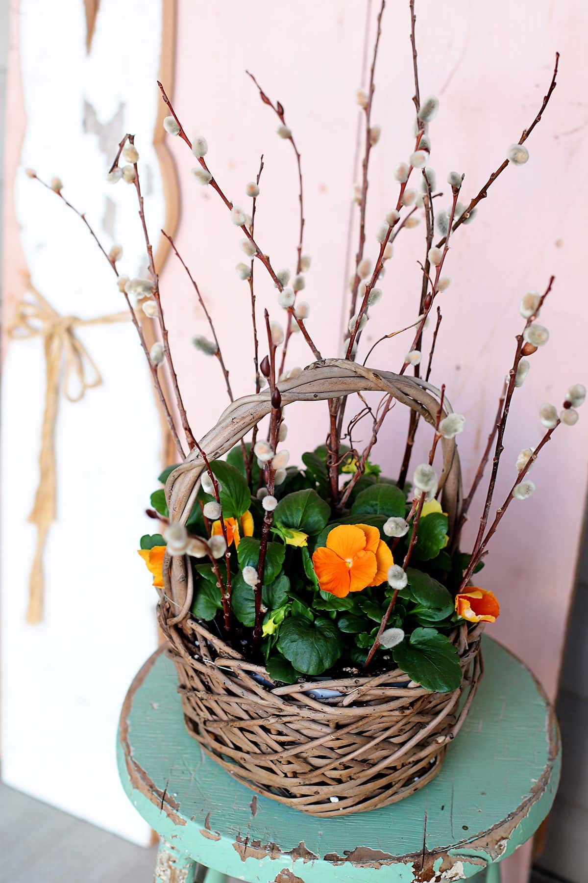 Basket of yellow pansies and pussy willow branches setting on a chippy green farmhouse stool,