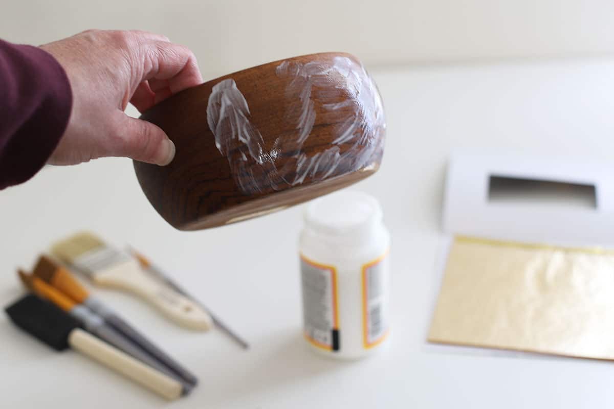 Mod Podge being applied to a wooden bowl which will be covered by gold leaf.